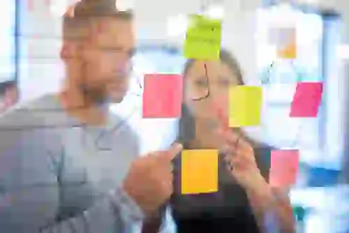 Team working on a transparent board, writing notes on post-its during workshop